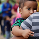 In this March 14, 2019 photo, a 7-month old boy peers over the shoulder of his mother as they wait for DHS agents to apprehend them at the U.S.-Mexico border near McAllen, Texas.
